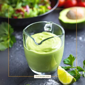 avocado salad dressing in a glass jug on a table with salad