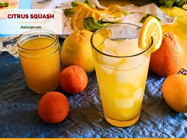 glass of citrus squash on a table surrounded by citrus fruit